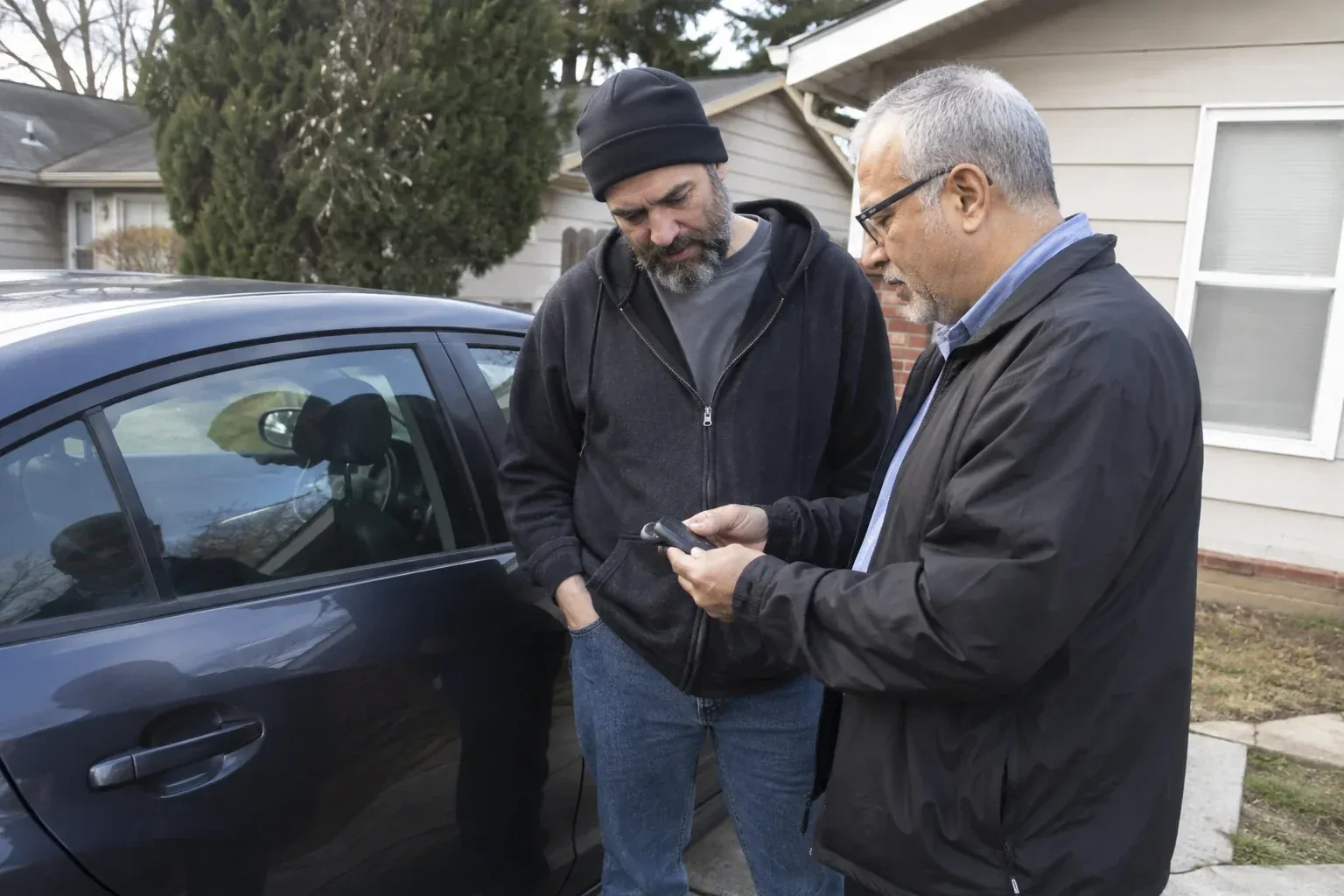 Two adults discussing a key fob beside a parked car. — Car Lockout Service, Brampton